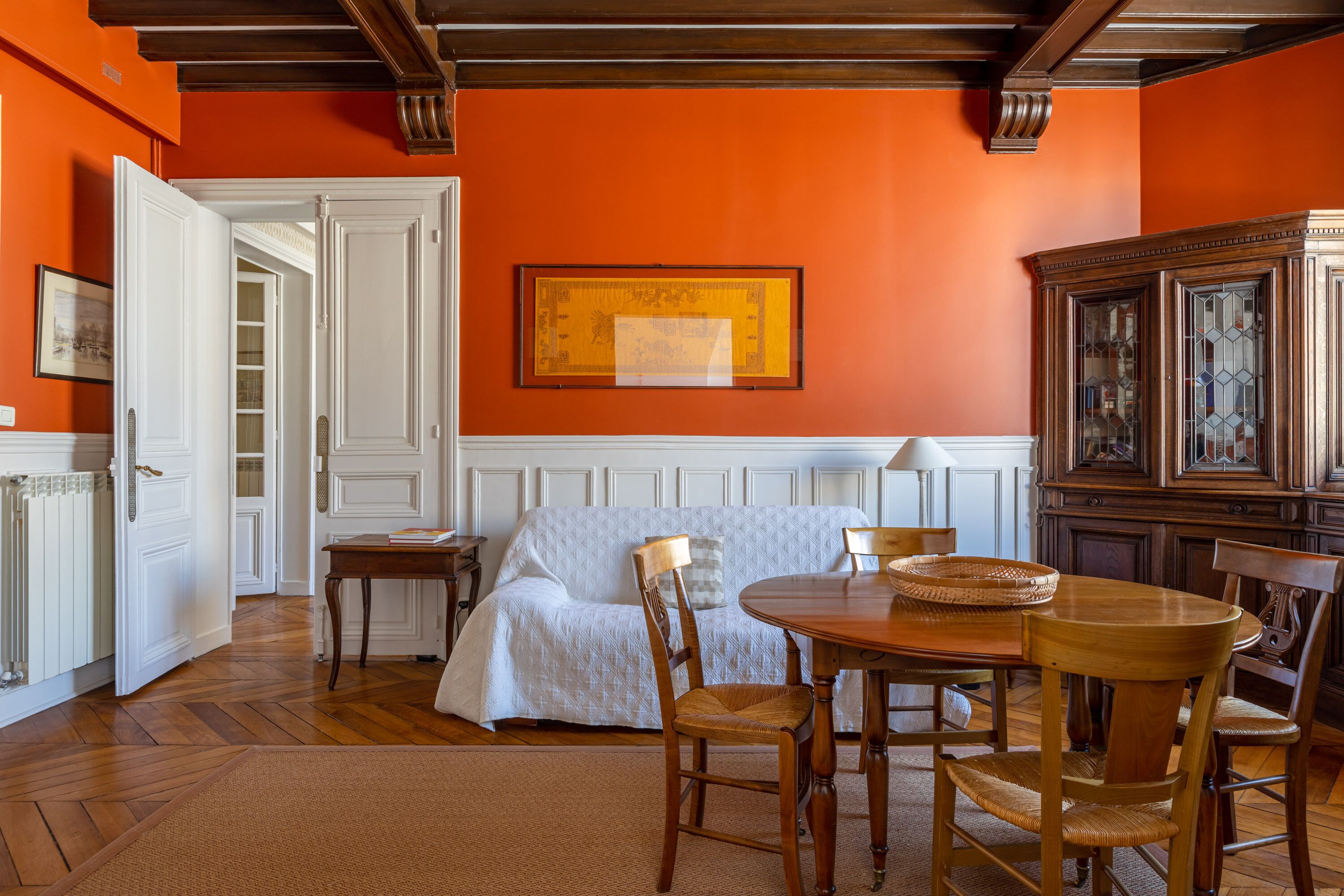 A room with a wooden dining table, chairs, a white sofa, and a large framed picture on the wall.