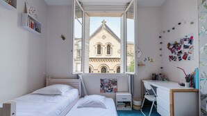 Un dormitorio con dos camas, un escritorio y una ventana con vista a un edificio.