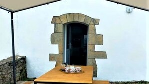 A wooden table with benches under a tent, a stone archway, and a stone wall.