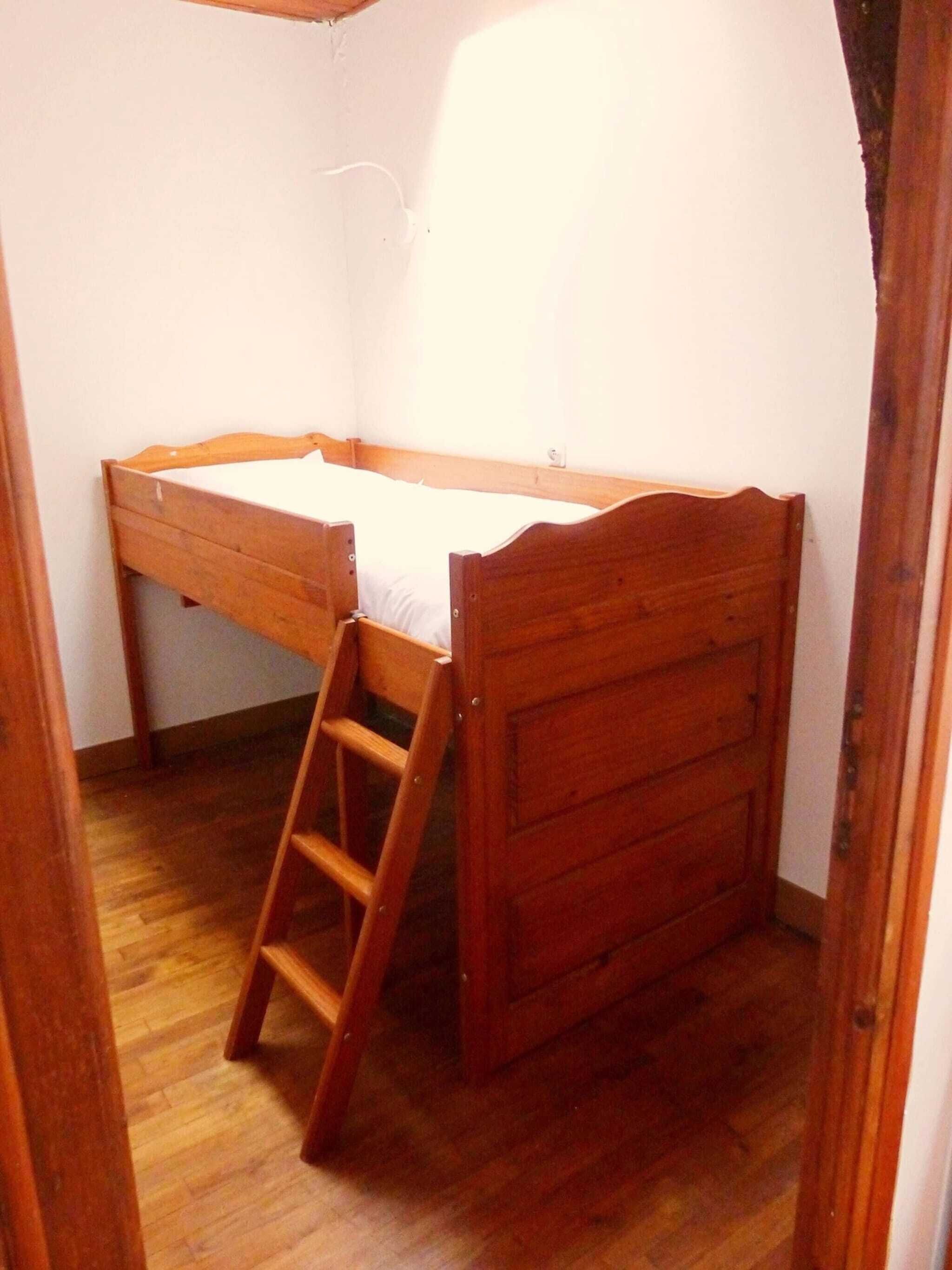 Ein kleines Zimmer mit einem Einzelbett, einer Holzleiter und einem schlichten Bettgestell aus Holz.