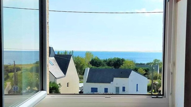 A window with a view of a coastal area, including houses and the sea.