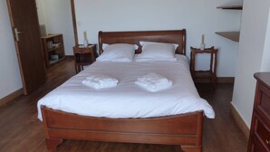 A neatly made bed with white linens and two towels, wooden headboard, two bedside tables with lamps, and a wooden wardrobe.