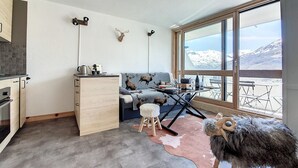 A cozy room with a sofa, a small table, a wooden cabinet, and a large window with a mountain view. - Modern 3-room apartment, ski-in/ski-out, balcony, exceptional view (Les Menuires)