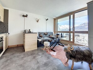 Une pièce confortable avec un canapé, une petite table, un meuble en bois et une grande fenêtre donnant sur les montagnes.