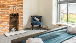 A room with a brick fireplace, a blue armchair, a bed with blue and white bedding, and a window with a view of houses. - 7 Severn Terrace (Watchet)