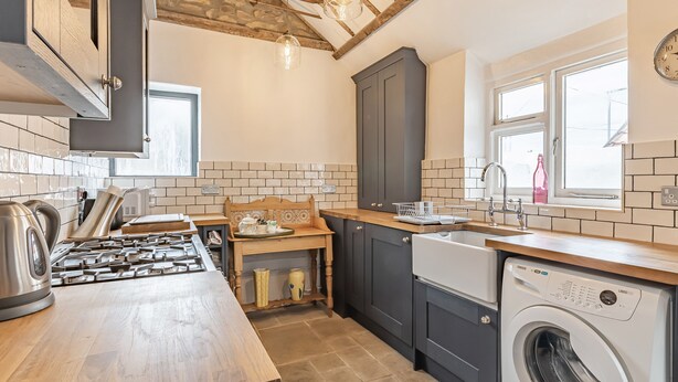 A modern kitchen with a wooden countertop, built-in appliances, and a stone wall backsplash. - 7 Severn Terrace (Watchet)