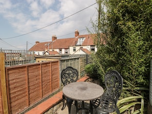 A patio with a round table and two chairs, surrounded by a wooden fence and greenery.