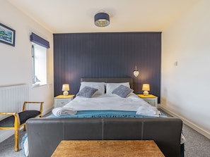A neatly made bed with white linens and two pillows, flanked by bedside tables with lamps, in a room with dark wooden paneling and a window with a view.