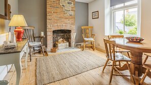 A cozy room with a brick fireplace, wooden furniture, and a large window. - 7 Severn Terrace (Watchet)