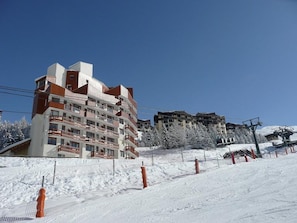 A multi-story hotel with balconies, located in a snowy area with ski slopes in the background.