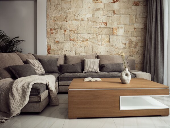A modern living room with a stone wall, a sectional sofa, a coffee table, and a potted plant.