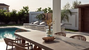 A poolside area with a table, chairs, and lounge chairs. - Anthis Luxury Villas - 3 Bedroom Villas with Private Pool (Zakynthos)