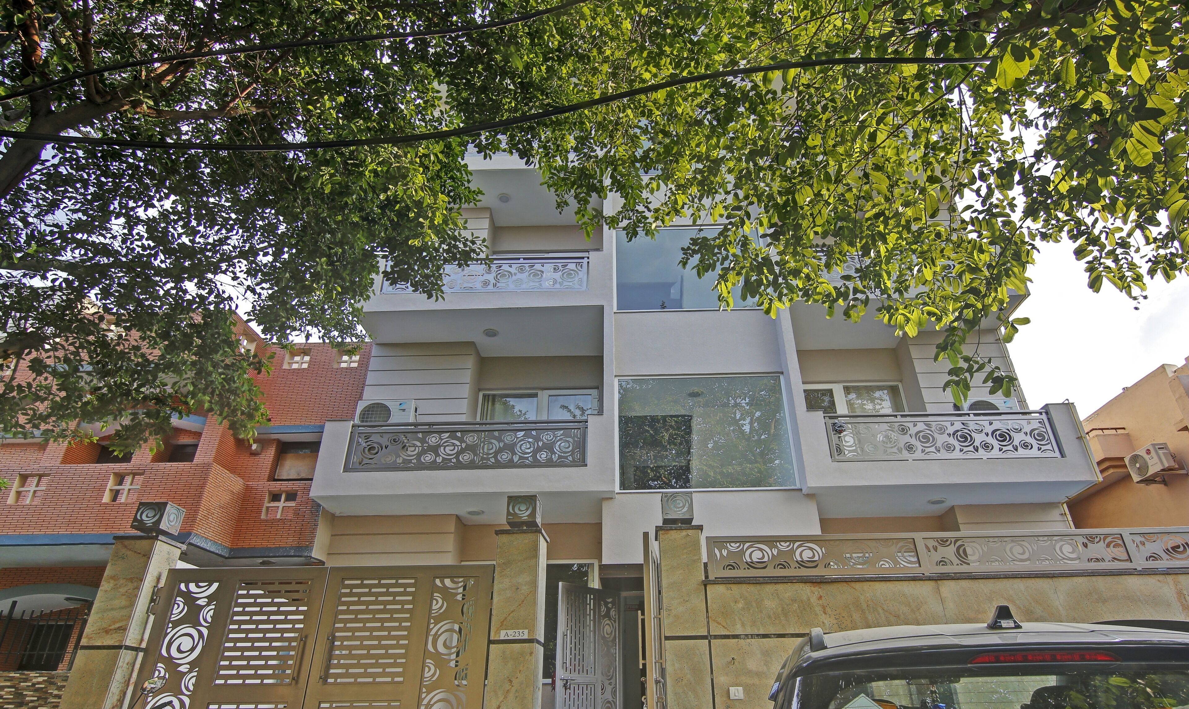 A multi-story residential building with balconies, a gated entrance, and a car parked in front.