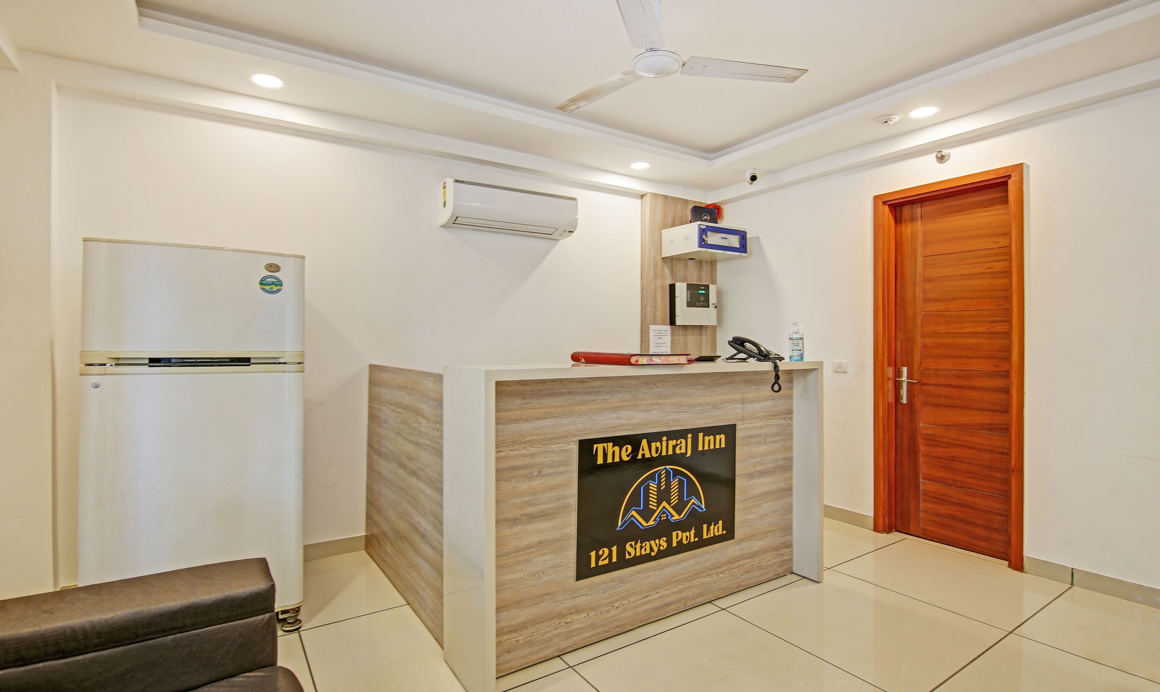 A reception desk with a sign for The Aviraj Inn, a refrigerator, a phone, and a wooden door.