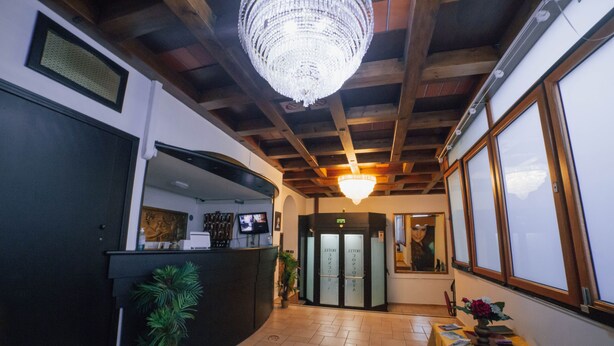 A lobby with a reception desk, a chandelier, a plant, and a table with books. - hotel Concordia s.n.c. (Crotone)