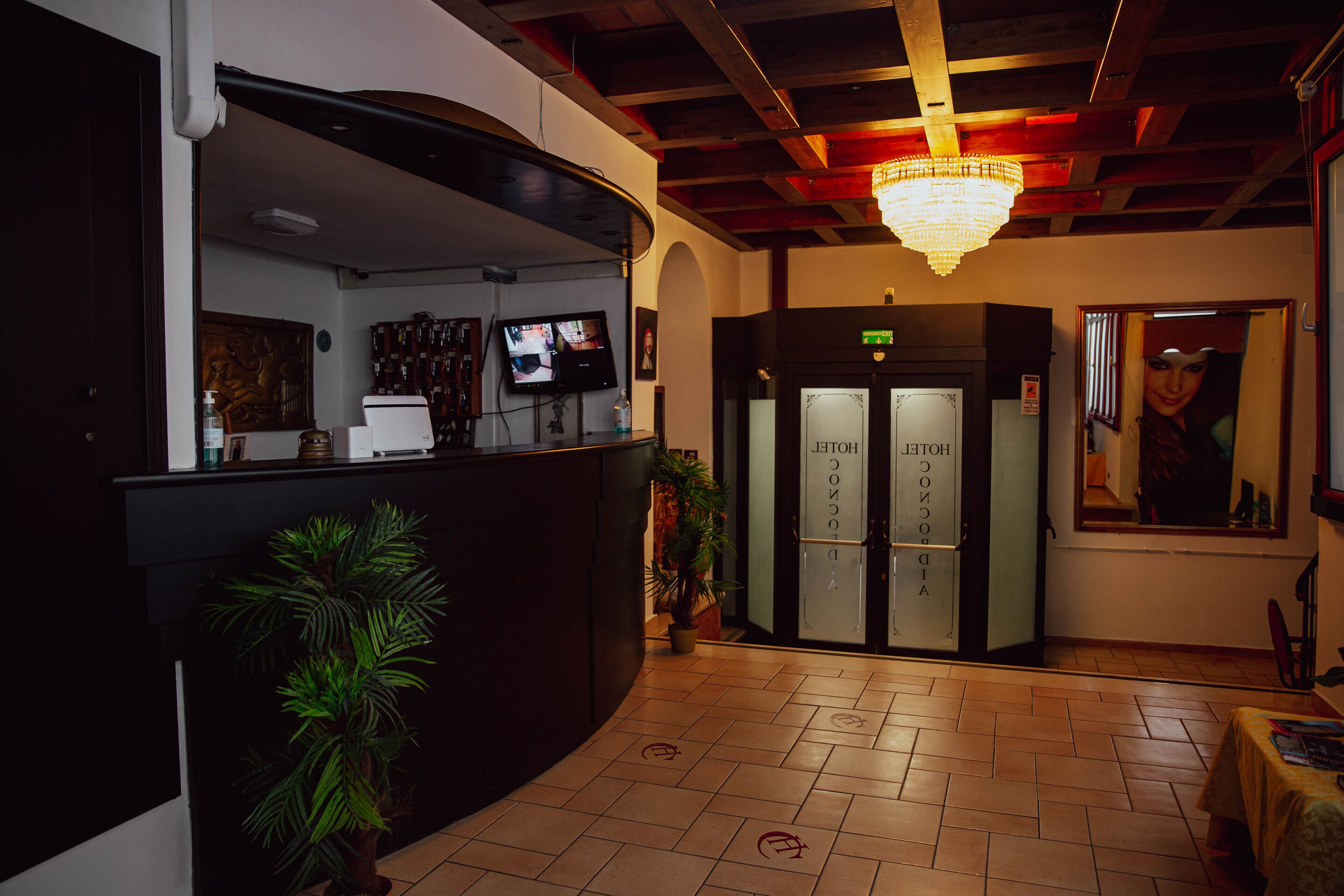A hotel reception area with a curved counter, a television screen, a chandelier, and a door marked "HOTEL".