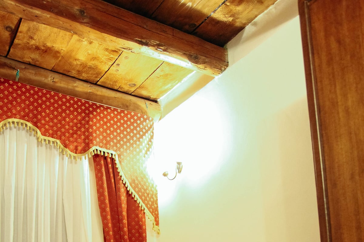 A room with a bed, wooden ceiling, and curtains.