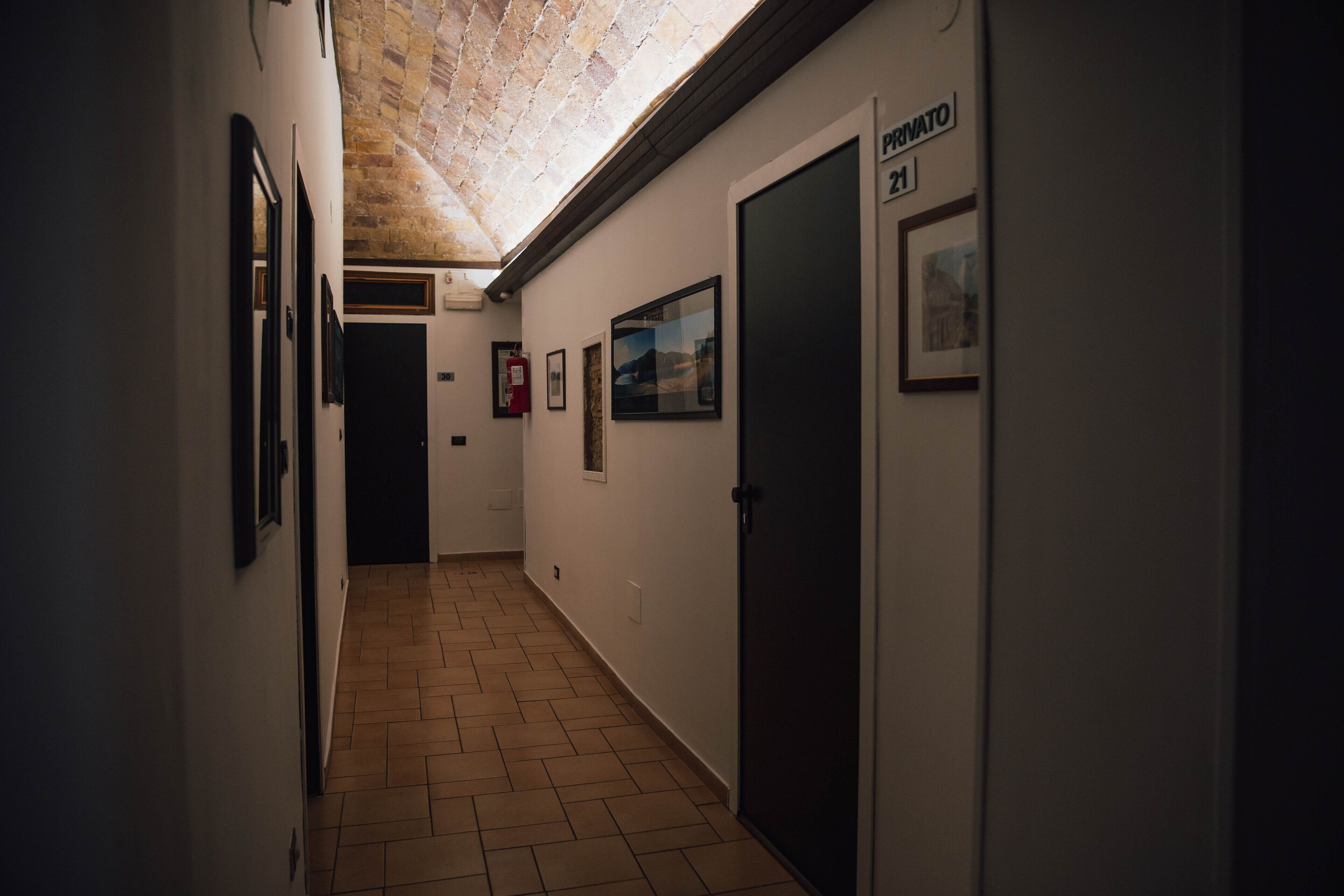 A narrow hallway with tiled flooring, framed pictures on the walls, and a door labeled "Privato 21".