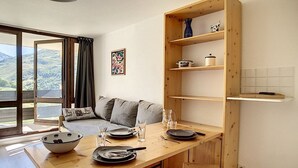 Una cocina moderna con armarios de madera, una mesa de comedor para dos personas y vistas al exterior a través de grandes ventanales.