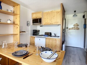 Een compacte keuken met houten kastjes, een magnetron, een koffiezetapparaat en een kleine koelkast.