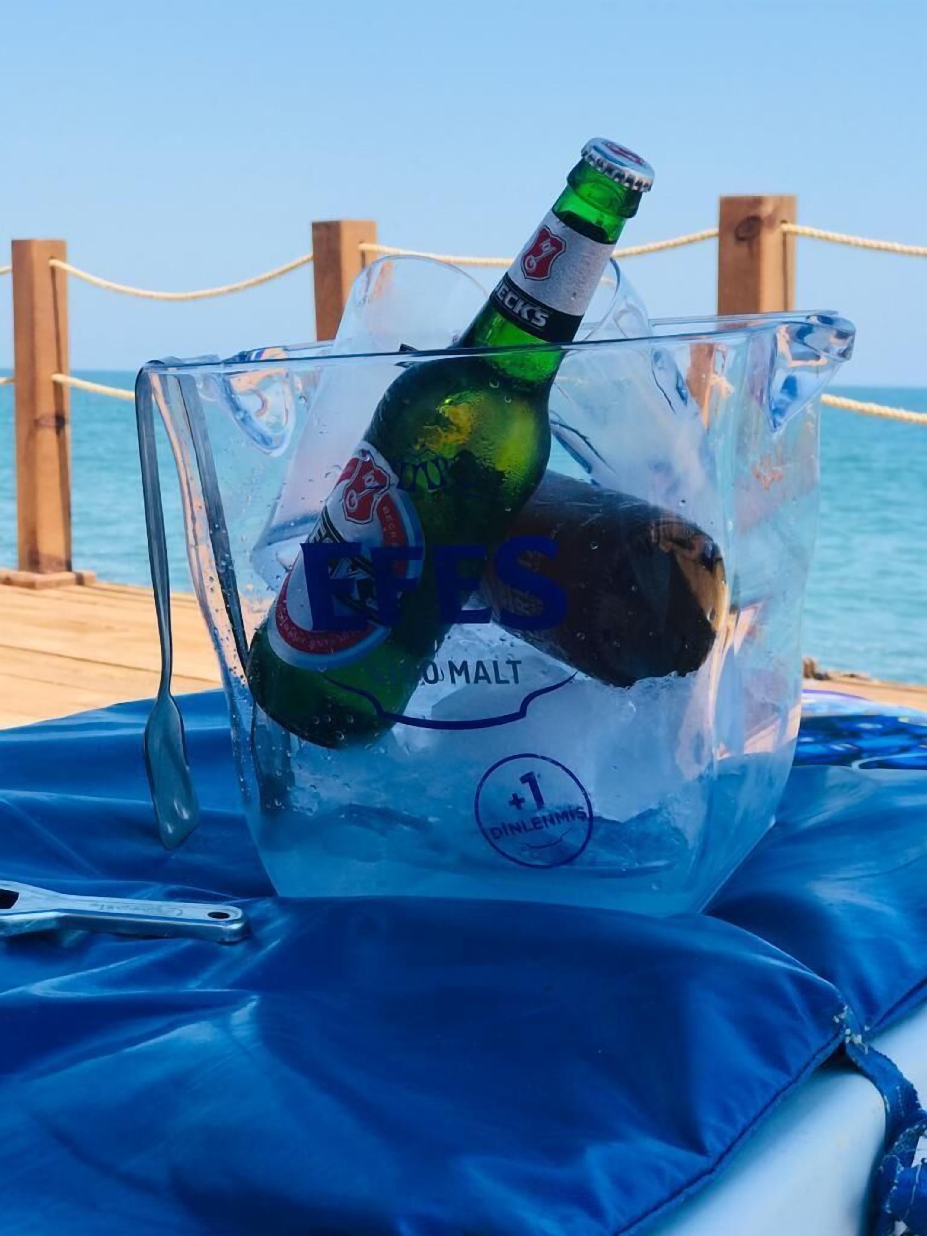 Eine Bierflasche in einem klaren Plastikeimer vor einem Holzhintergrund mit einer Seilsperre.