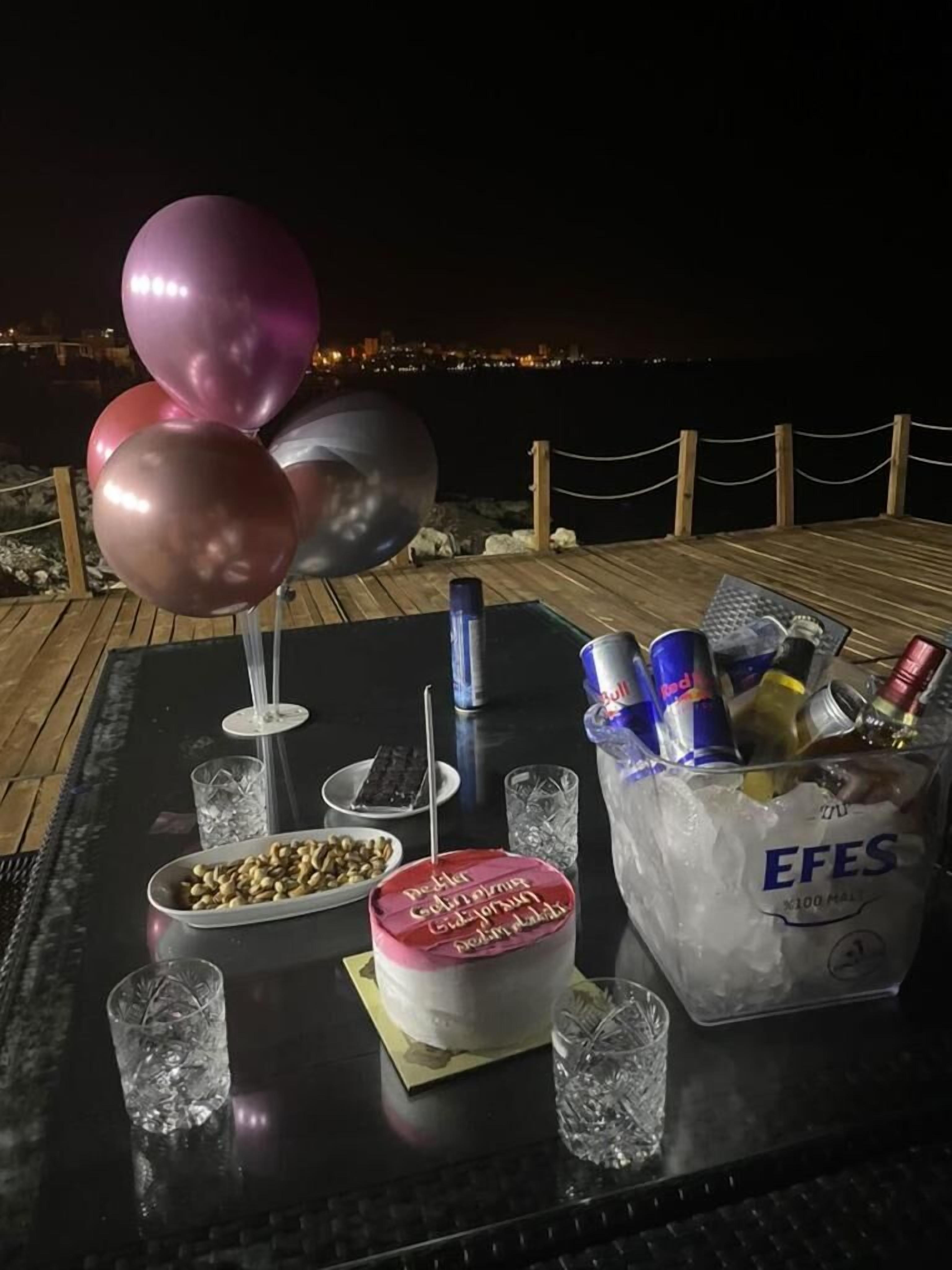 A table set with a dessert, balloons, snacks, drinks, and a view of the city at night.