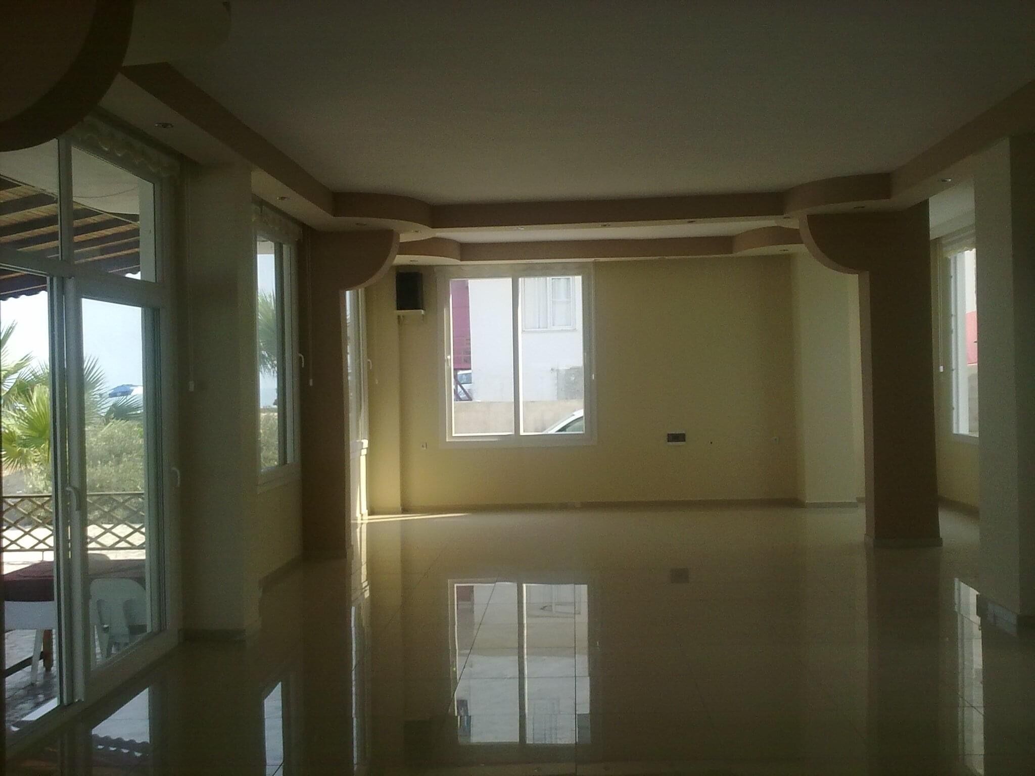 Ein geräumiges Zimmer mit großen Fenstern, einem Balkon und einem Fliesenboden.