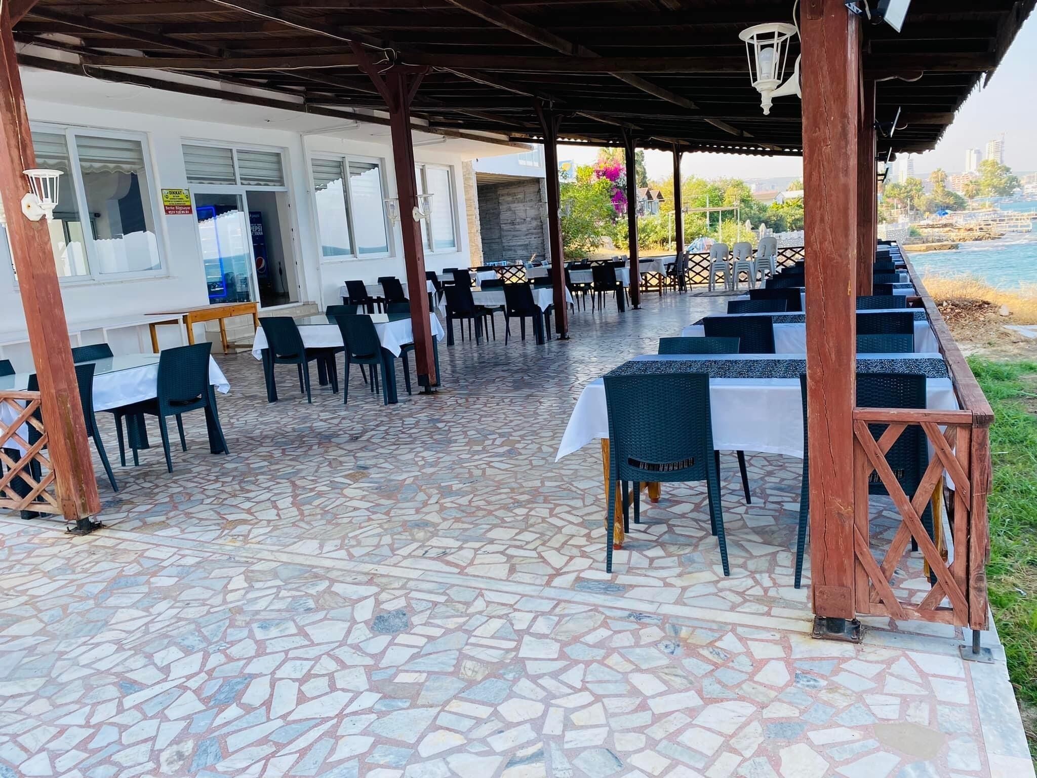 Un área de comedor al aire libre con suelo de losas de piedra, mesas con manteles blancos y sillas.