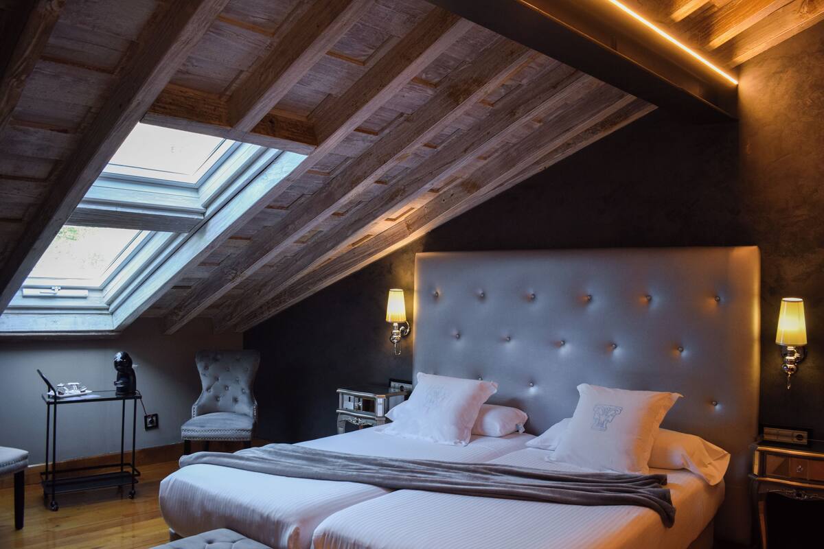 A bedroom with a large bed, a chair, a desk, and a skylight.