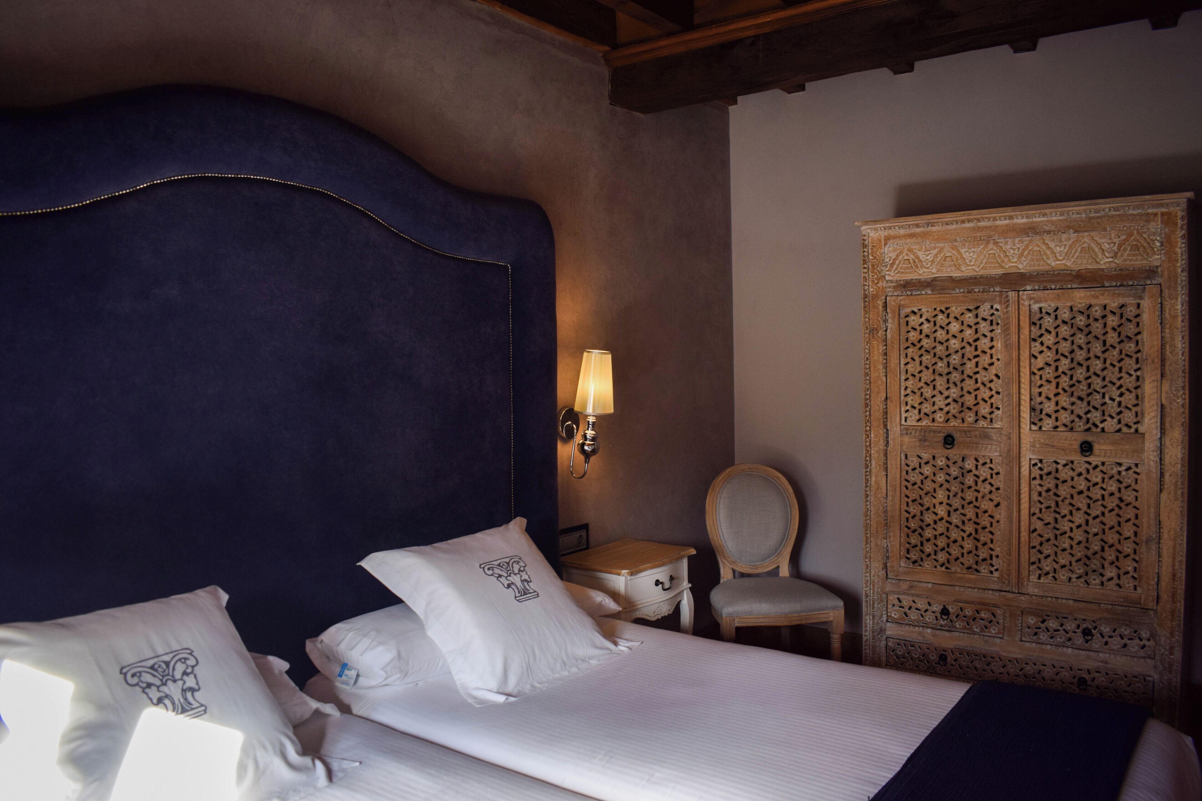 A hotel room with a large bed, a wooden wardrobe, a nightstand, and a chair.