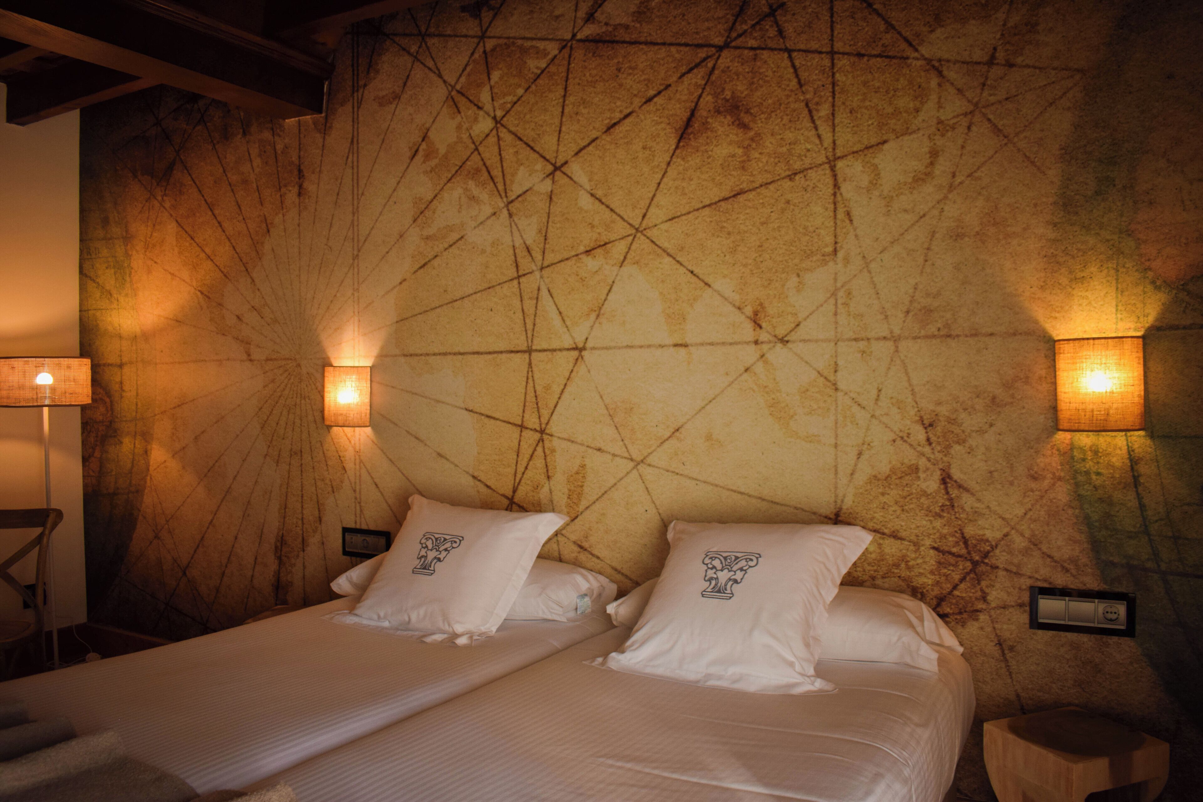 Habitación de hotel con dos camas, cada una con ropa de cama blanca y almohadas a juego, una pared con textura y dos lámparas de pared.