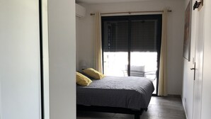A bedroom with a bed, a window with curtains, a mirror, and a door. - T4 Sainte Anne - Fonds Thezan (Sainte-Anne)