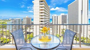 A balcony with a glass table, two chairs, and a vase with flowers.