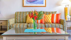 A room with a sofa, a glass coffee table, a vase with flowers, and a painting on the wall.