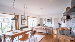 A modern kitchen with a wooden dining table, chairs, pendant lights, and a view of the outside.