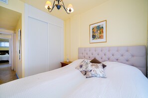 A bedroom with a large bed, a chandelier, a framed picture on the wall, and a wardrobe.