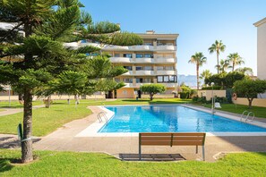 A swimming pool with a bench, surrounded by greenery and a multi-story building.