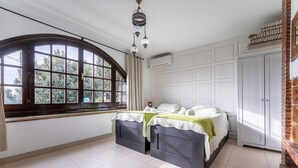 Ein Schlafzimmer mit einem großen Bogenfenster, einem Bett mit grüner Decke, einer hängenden Chandelieber und einem Kamin aus Ziegelsteinen.