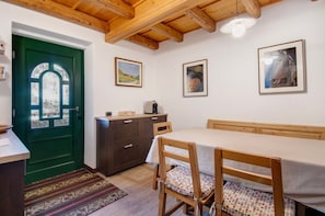 A room with a green door, wooden ceiling beams, a dining table with chairs, and framed pictures on the wall.