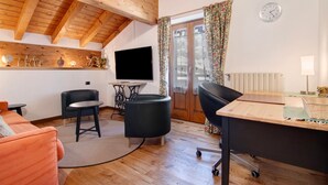 Een moderne woonkamer met een houten plafond, een flatscreen televisie, een bureau, een bank en een eettafel.