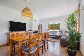 Een eetgedeelte met een houten tafel en stoelen, een televisie en een grote plant.
