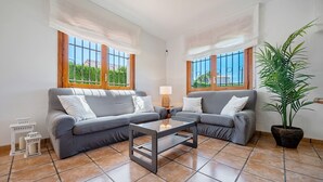 A living room with two grey sofas, a glass coffee table, a lamp, and a potted plant.