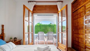 A bedroom with a bed, a wooden door, and a view of an outdoor seating area.