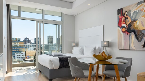 Een moderne slaapkamer met een groot bed, een glazen tafel en uitzicht op de stad.