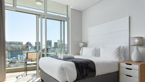 Een moderne slaapkamer met een groot bed, bedlampjes en uitzicht op de stad door middel van kamerhoge ramen.