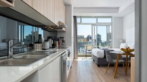 Een moderne keuken met een vaatwasser, spoelbak en koffiezetapparaat. Er is een eethoek met een tafel en stoelen. De kamer heeft grote ramen met uitzicht op de stad.