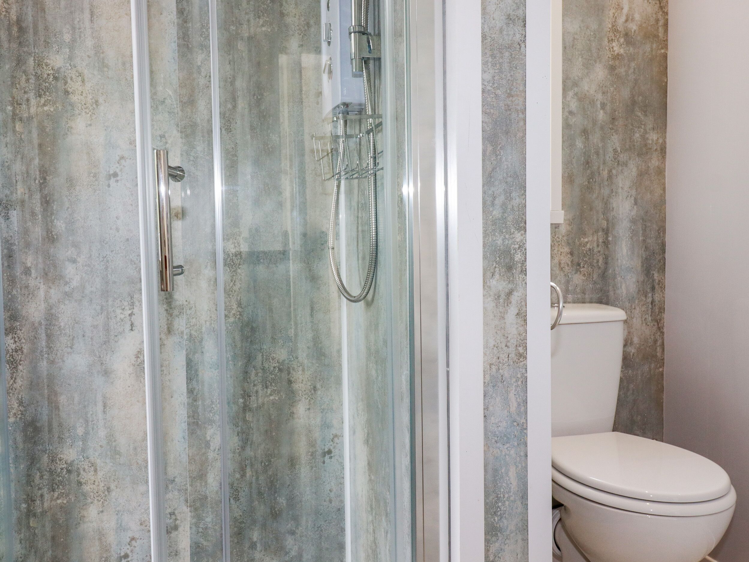 A bathroom with a glass-enclosed shower, a toilet, and a concrete-textured wall.