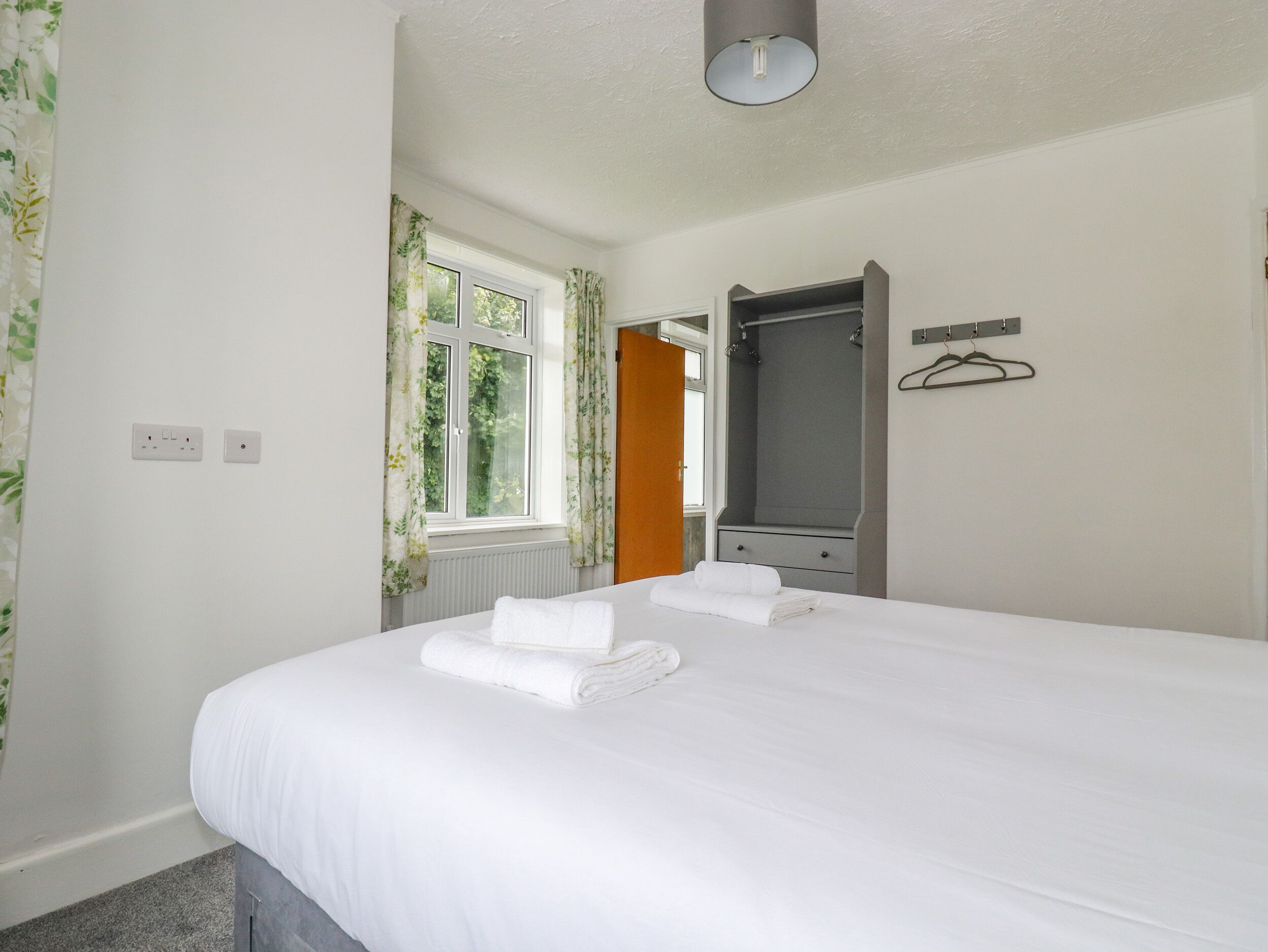 Hotellihuone, jossa on sänky, ikkuna verhoilla, peili ja pyyheteline.