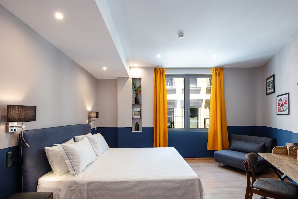 Une chambre d’hôtel avec un lit, un canapé, une table à manger et une fenêtre avec des rideaux.