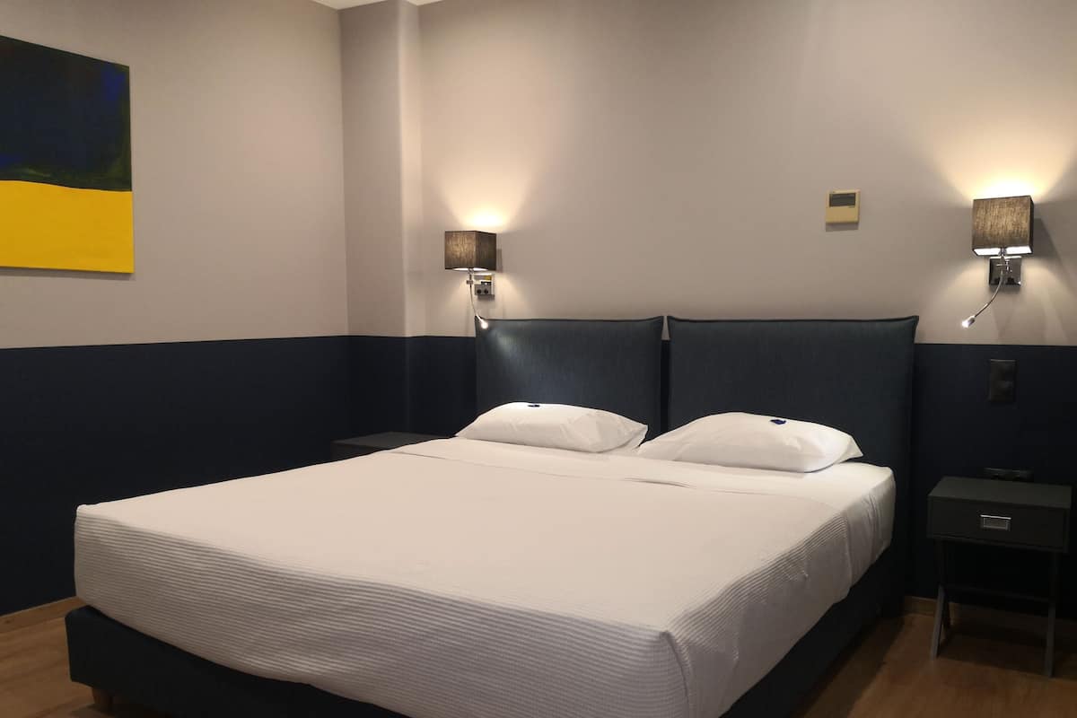 Une chambre d’hôtel avec un grand lit, deux tables de chevet et des lampes fixées au mur.